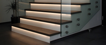 Eine Treppe mit Treppenstufen aus Holz, einem Glasgeländer und LED-Leuchten.
