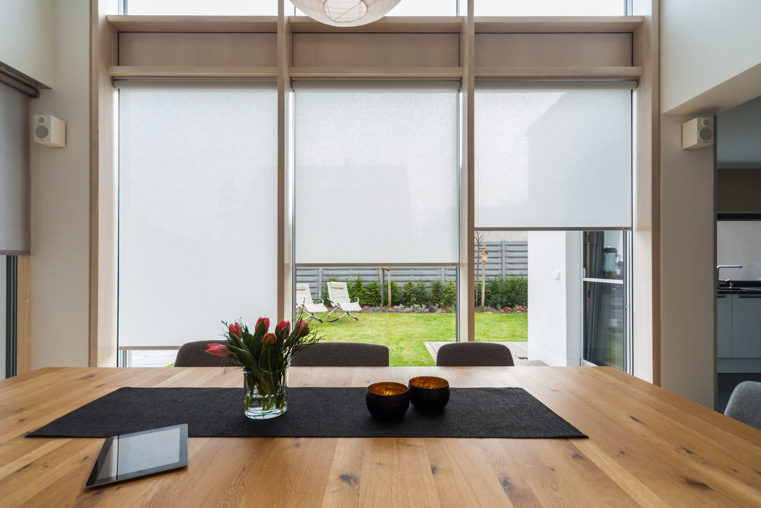 Modernes Esszimmer mit raumhohen Fenstern an denen Sonnenschutzrollos befestigt sind.